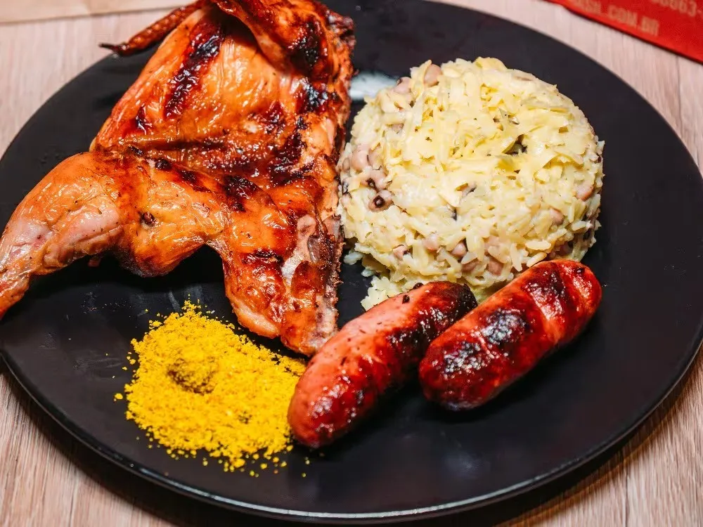Meio galeto assado servido no prato com linguiça e acompanhamentos